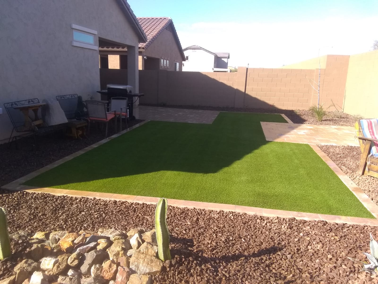 Verrado backyard turf and paver patio design with travertine border and desert rockwork