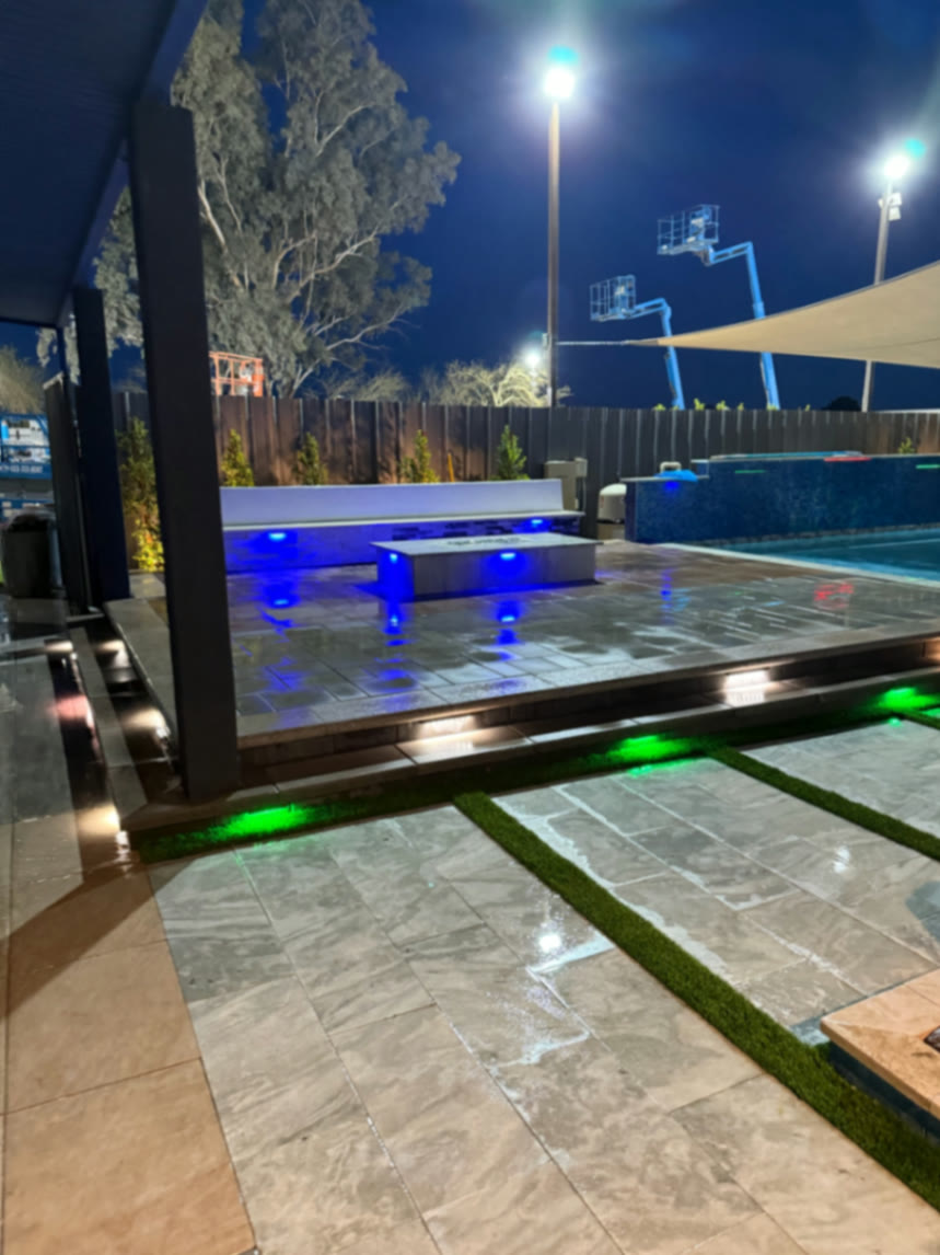 Raised pool deck with blue bench lighting, green path lights, and large-format pavers after dark