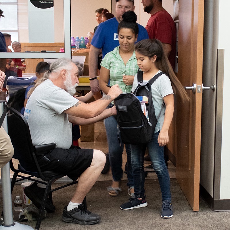 Volunteer kneeling to help a young girl adjust the straps on her new backpack