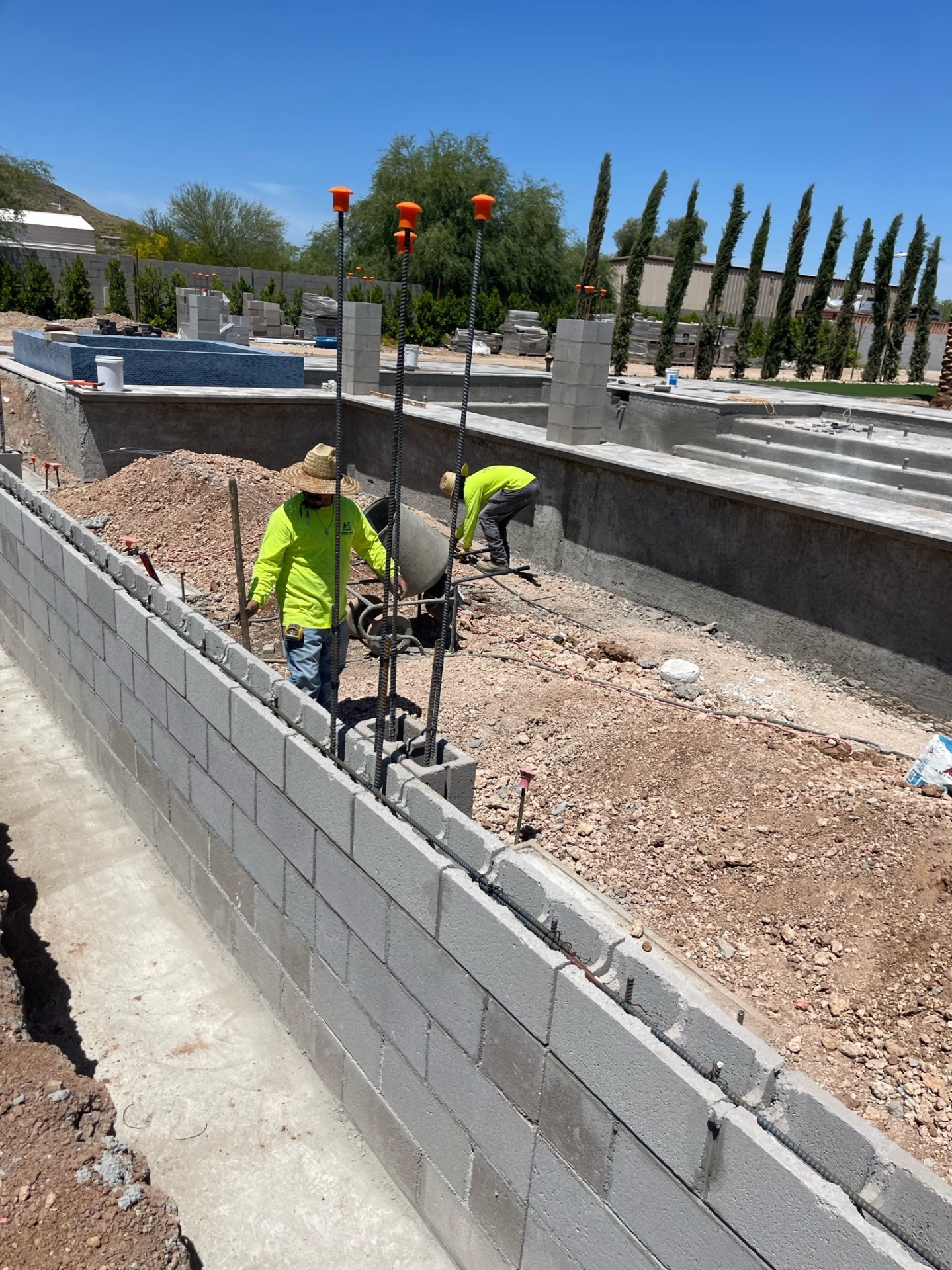 AE crew tying rebar and laying block on a tall perimeter wall with the gunite pool shell and raised tiled spa already in place