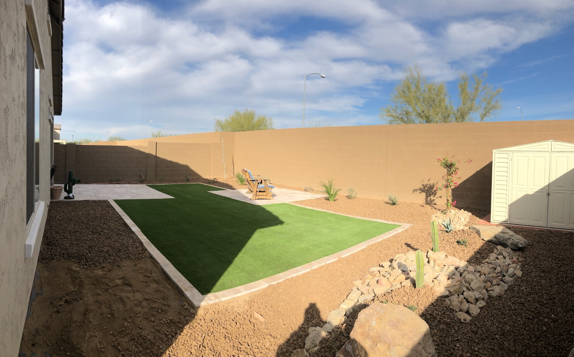 Verrado backyard artificial turf lawn with travertine paver border along a corner-lot property