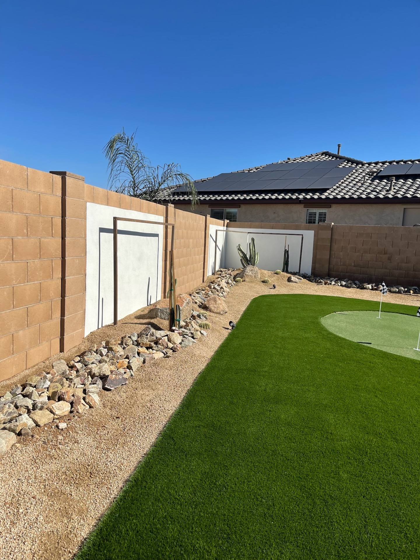 Goodyear backyard artificial turf lawn with putting green, cactus and boulder desert border along block wall