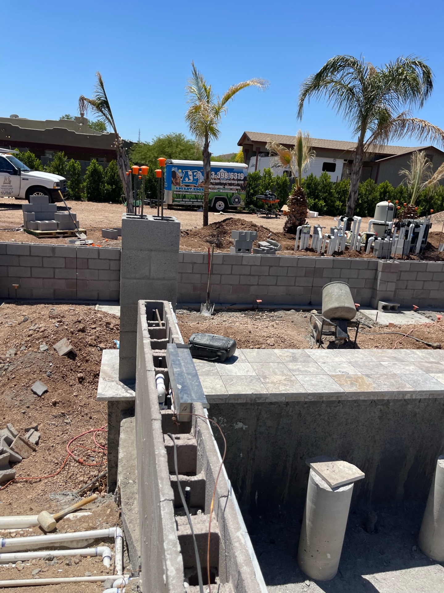 Raised block wall and open pool shell with AE truck and trailer parked beyond the backyard wall during mid-build