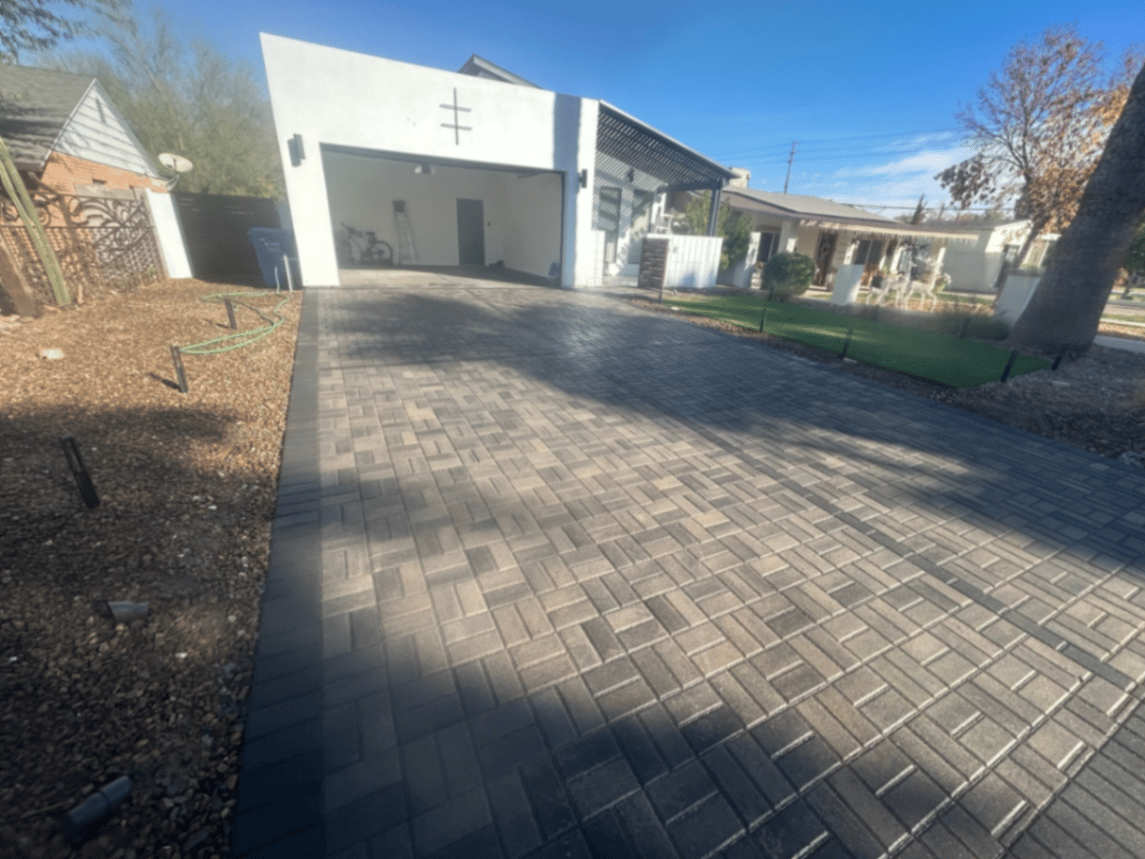 Charcoal paver driveway with sailor-course border serving a modern white stucco home.