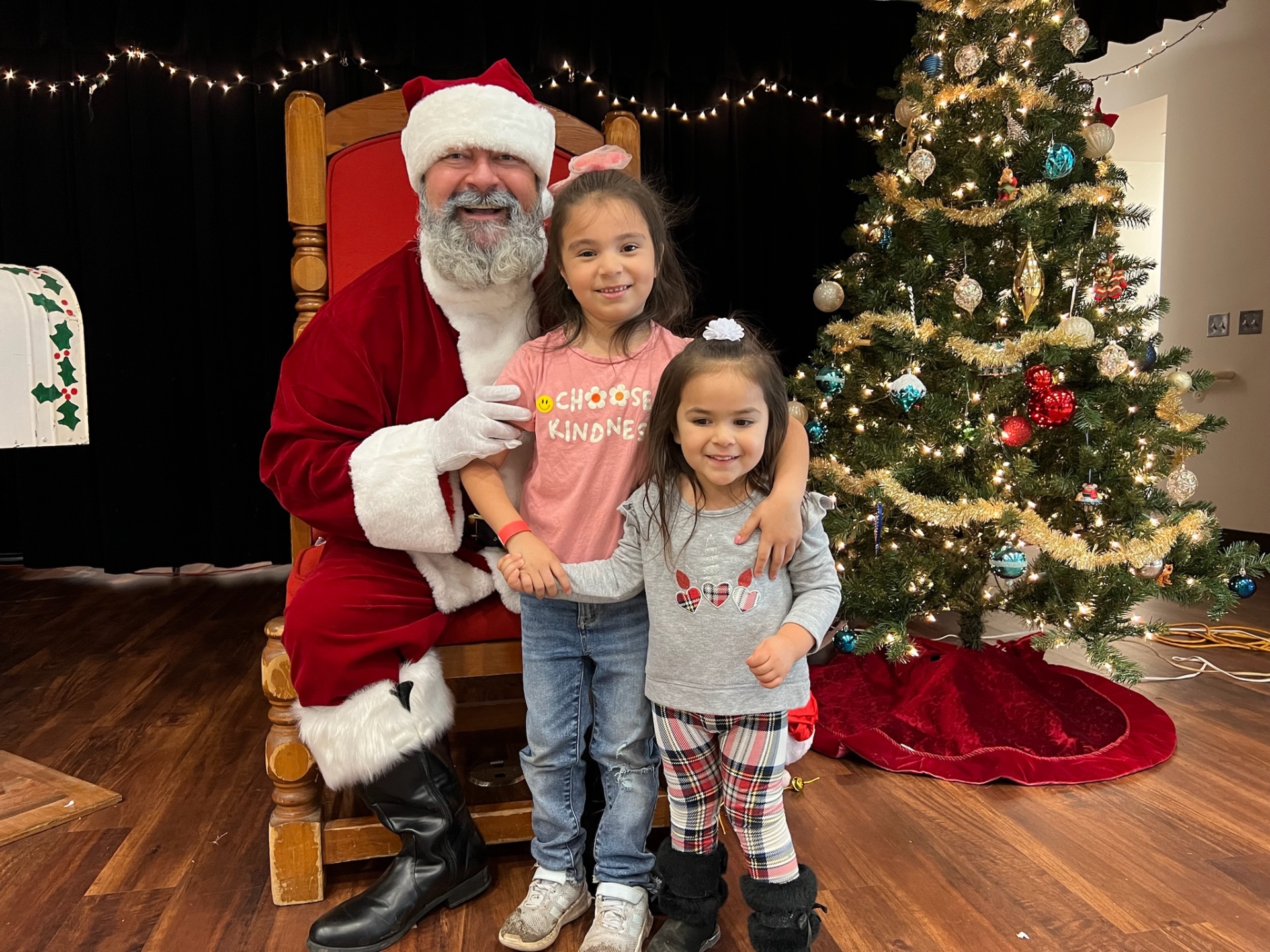 Santa with two young sisters in front of a Christmas tree at Shop With a Cop