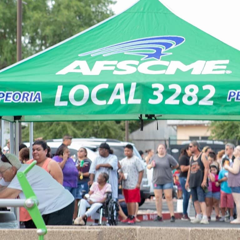 AFSCME Local 3282 tent with families gathered behind it during the backpack drive