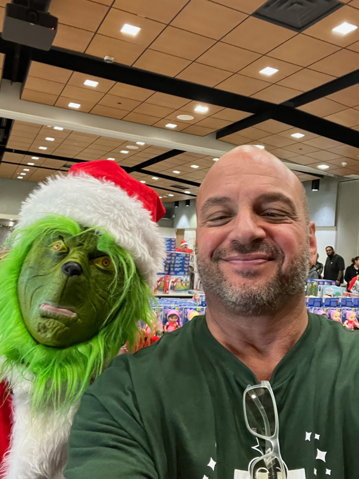 AE Outdoor Living team member taking a selfie with the Grinch in front of pallets of donated toys