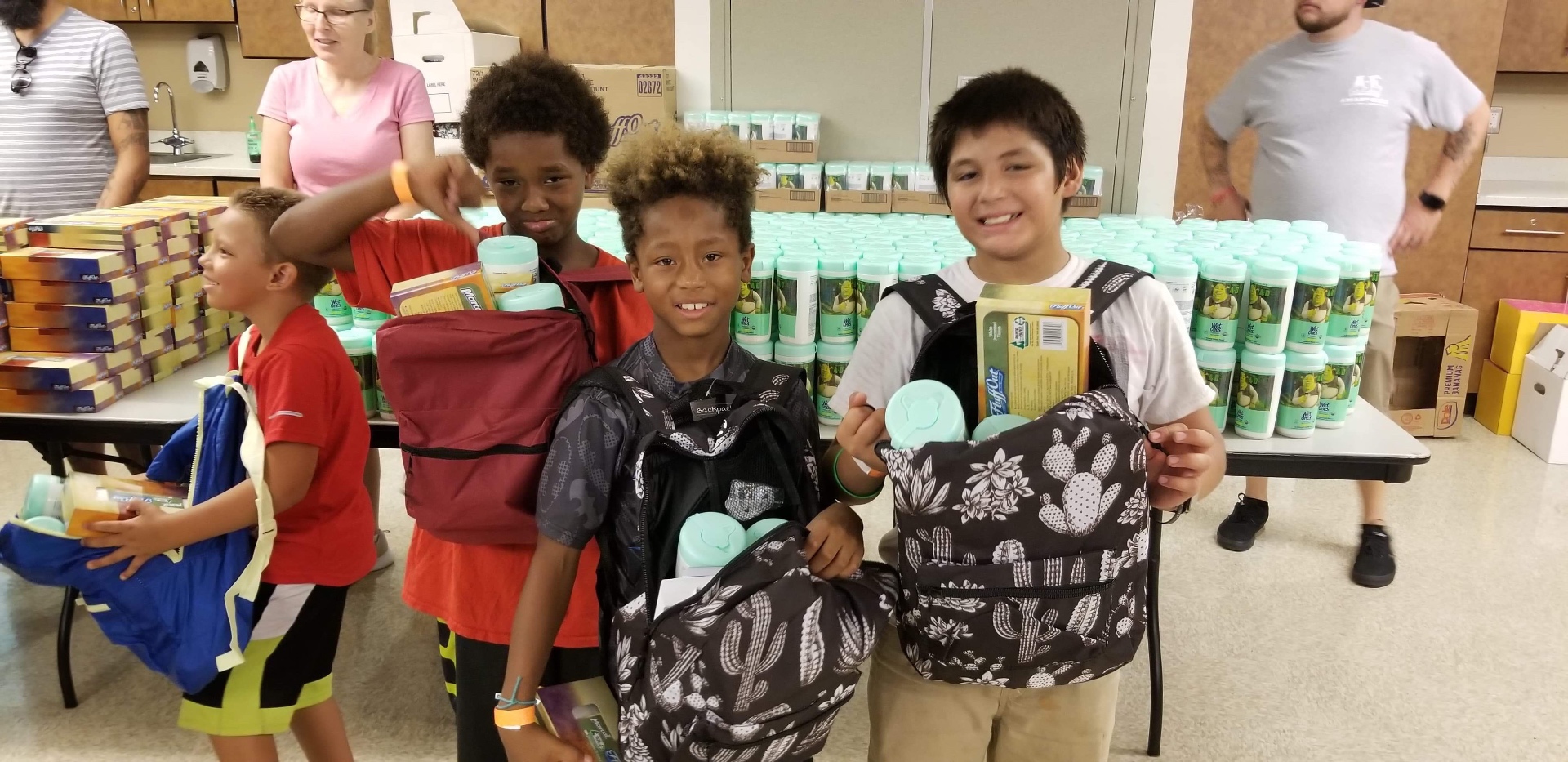 Four kids smiling with new backpacks and supplies at an AE Outdoor Living backpack distribution event