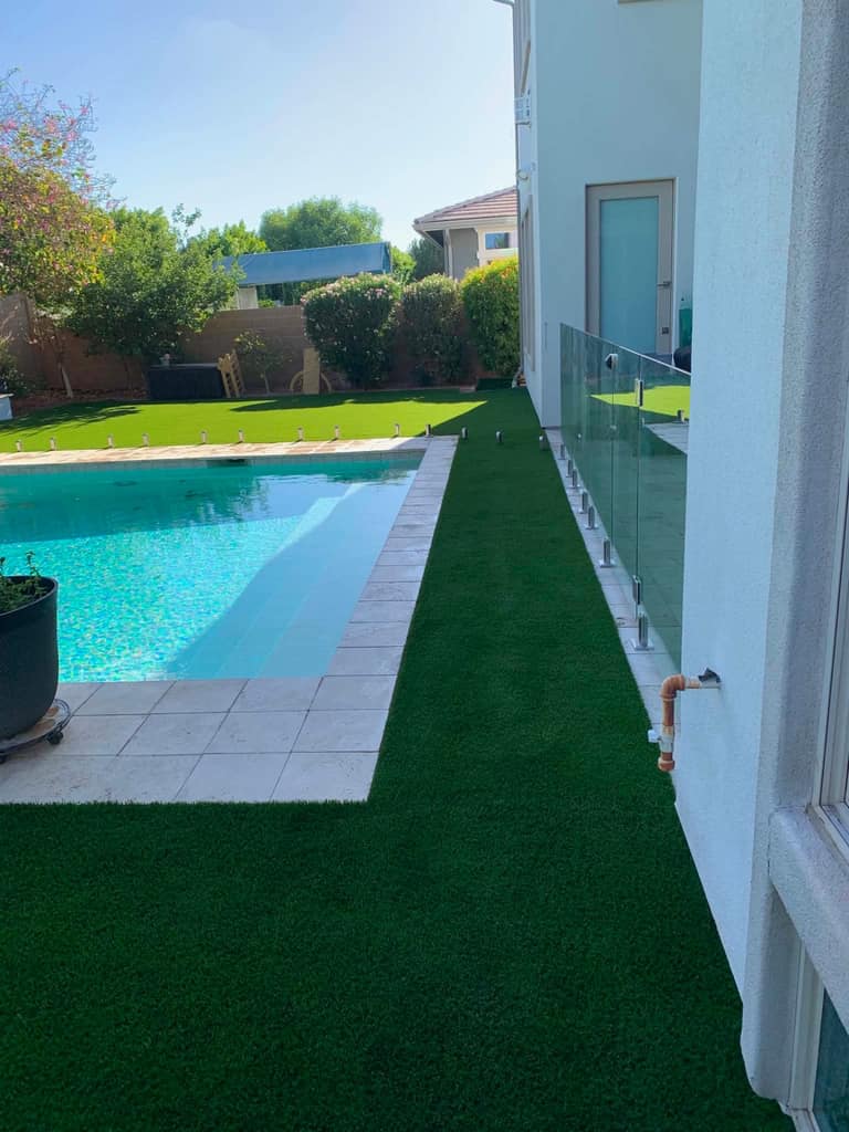 Narrow turf runner threaded between glass pool fence and the home — precision inset cuts.