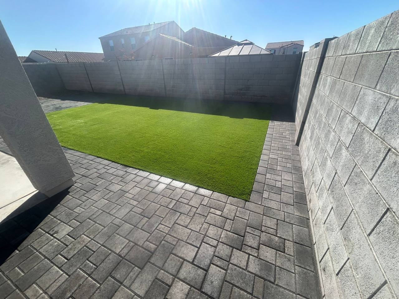 Rectangular artificial turf lawn framed by charcoal paver borders in a compact Arizona backyard