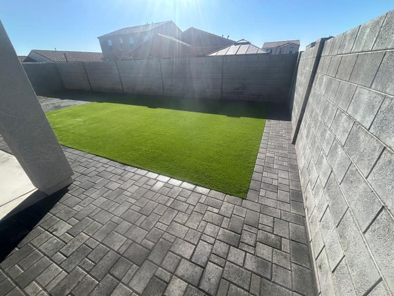 Rectangular artificial turf lawn framed by charcoal paver borders in a compact Arizona backyard