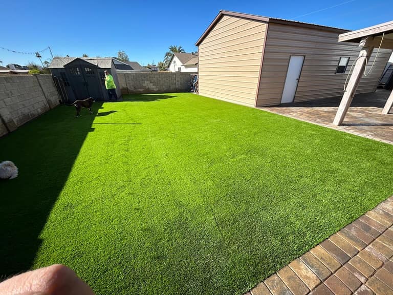 Pet-friendly turf lawn with tumbled paver border, sized for dogs to run between the house and shop.