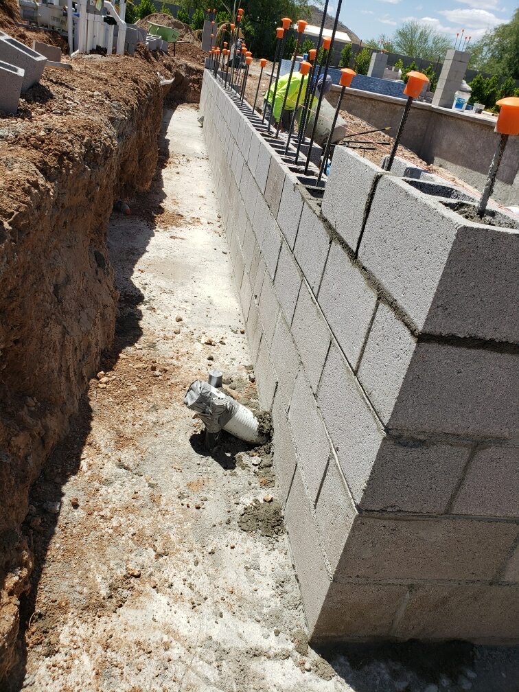 Freshly mortared CMU block wall with vertical rebar and plumbing stub-up along trench