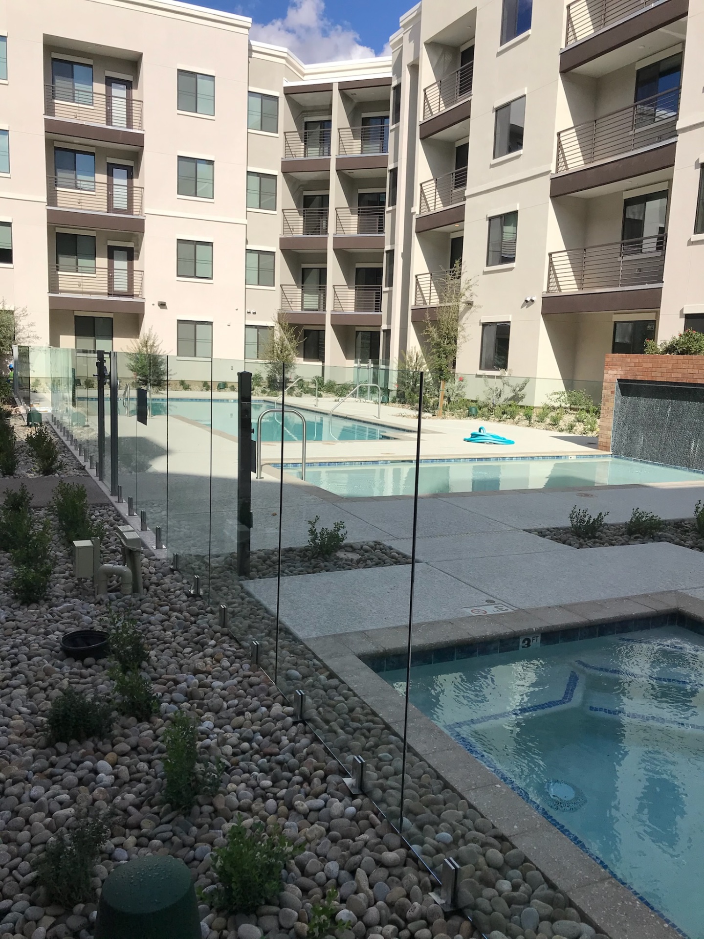 Wide view of a multifamily pool amenity enclosed with commercial frameless glass fencing and black access gate posts.