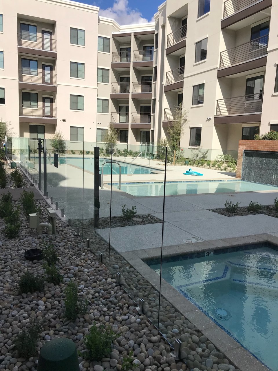 Wide view of a multifamily pool amenity bordered by frameless glass fence panels and dark gate posts.
