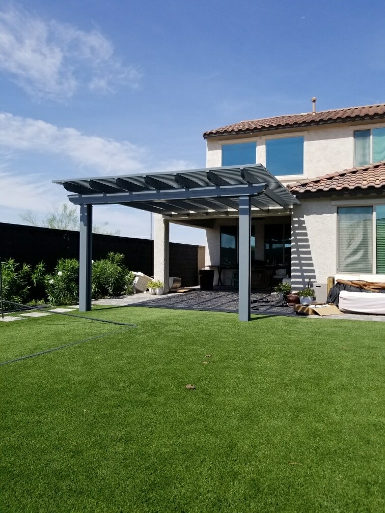 The Meadows (Peoria) freestanding grey alumawood lattice pergola with attached wall run, tile-paver patio and expansive artificial turf lawn against block wall by AE Outdoor Living