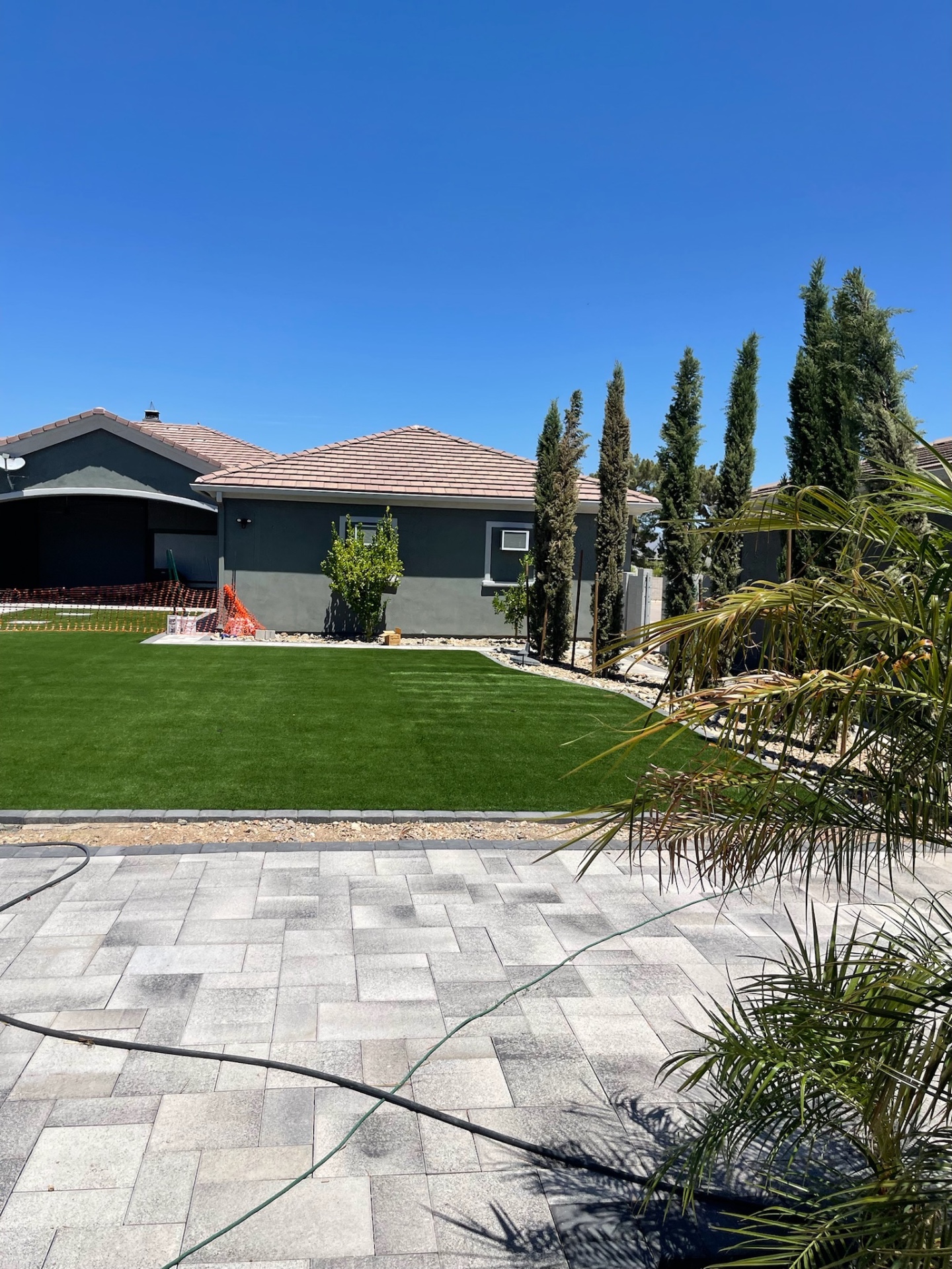 Finished side yard with crisp artificial turf, paver border, decorative gravel, Italian cypresses, and dark stucco home behind