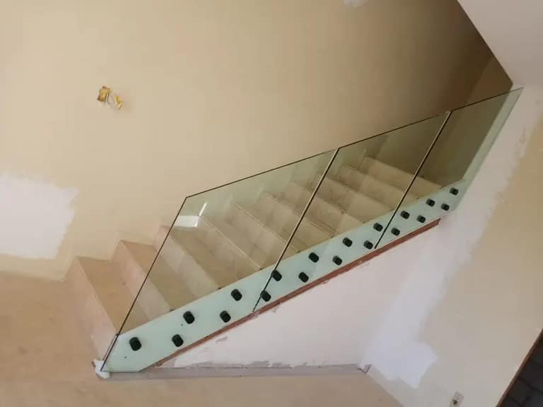 Interior staircase with frameless glass panels held by black base clips during installation.