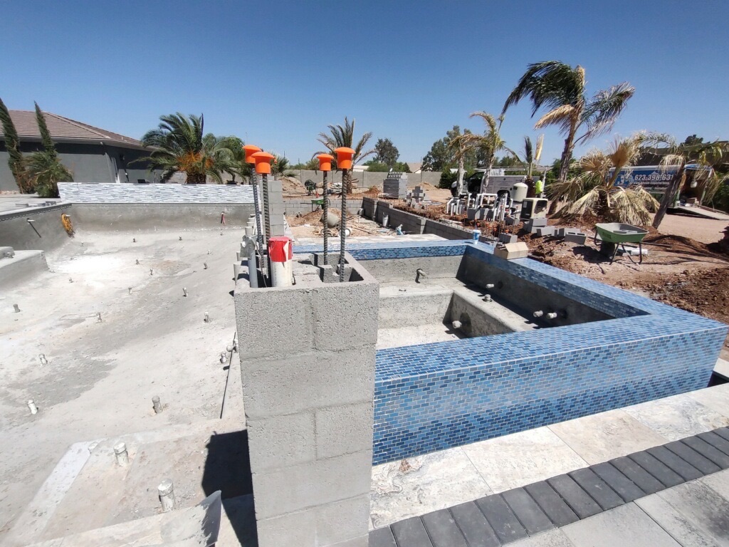 Blue mosaic glass tile spa with raised water-feature wall and pool shell beyond