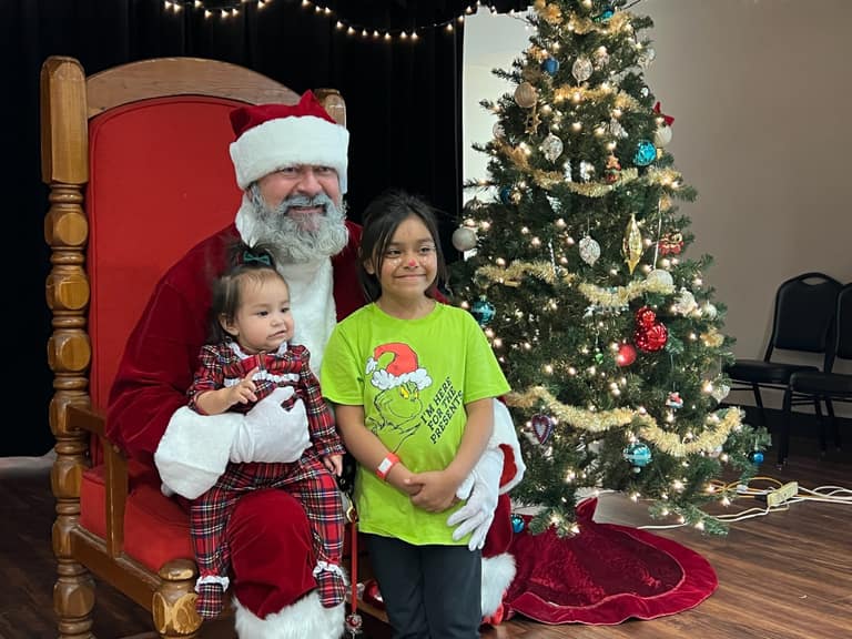 Santa with two sisters, one in a Grinch shirt, at Shop With a Cop event