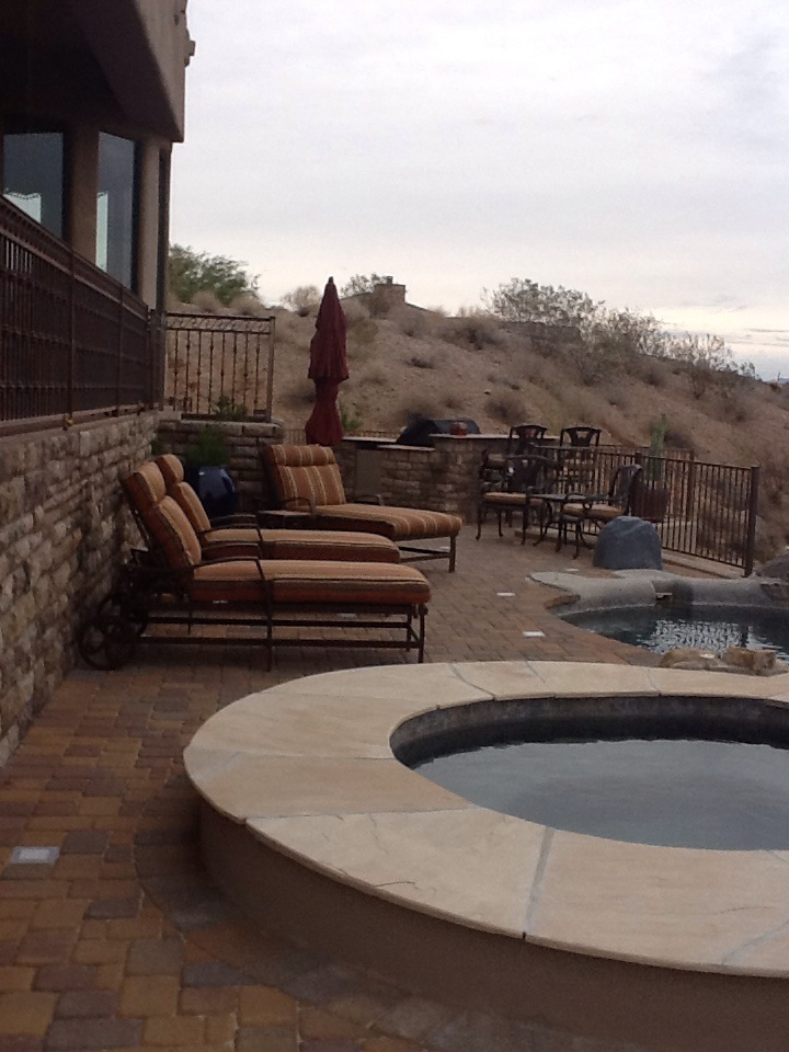 Fountain Hills paver pool deck at dusk with raised travertine spa, infinity pool edge and stacked-stone seat wall by AE Outdoor Living