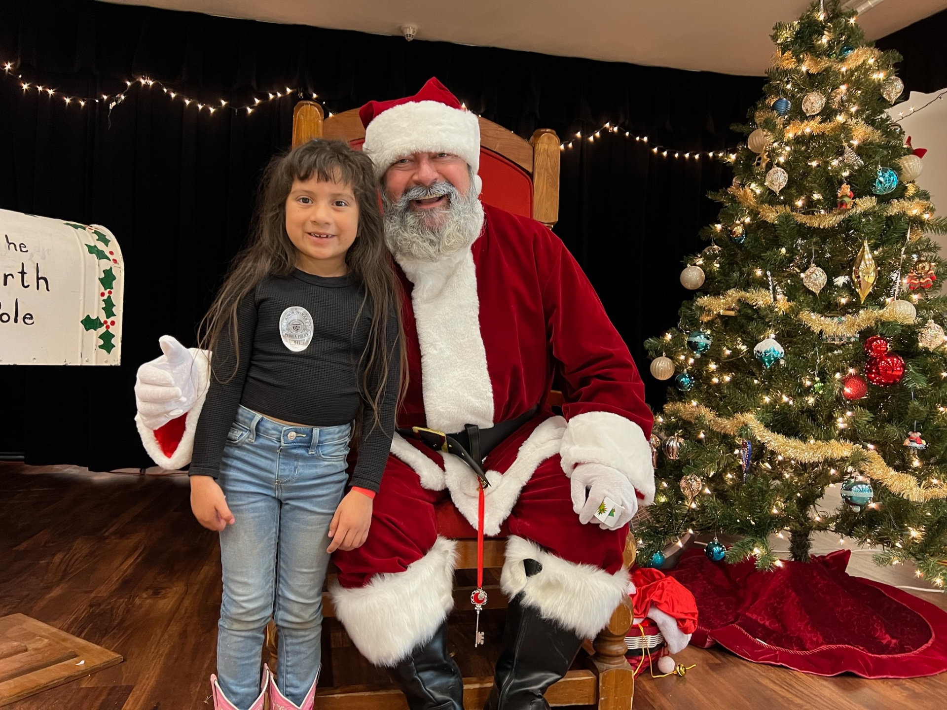 Young girl in a Peoria Police shirt posing with Santa at Shop With a Cop