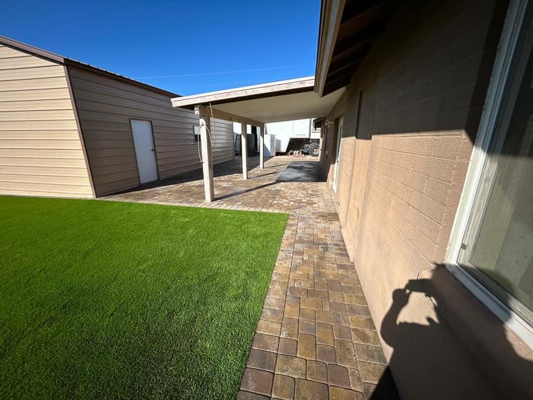 Paver walkway and turf tucked between house and detached shop, keeping the utility corridor usable.