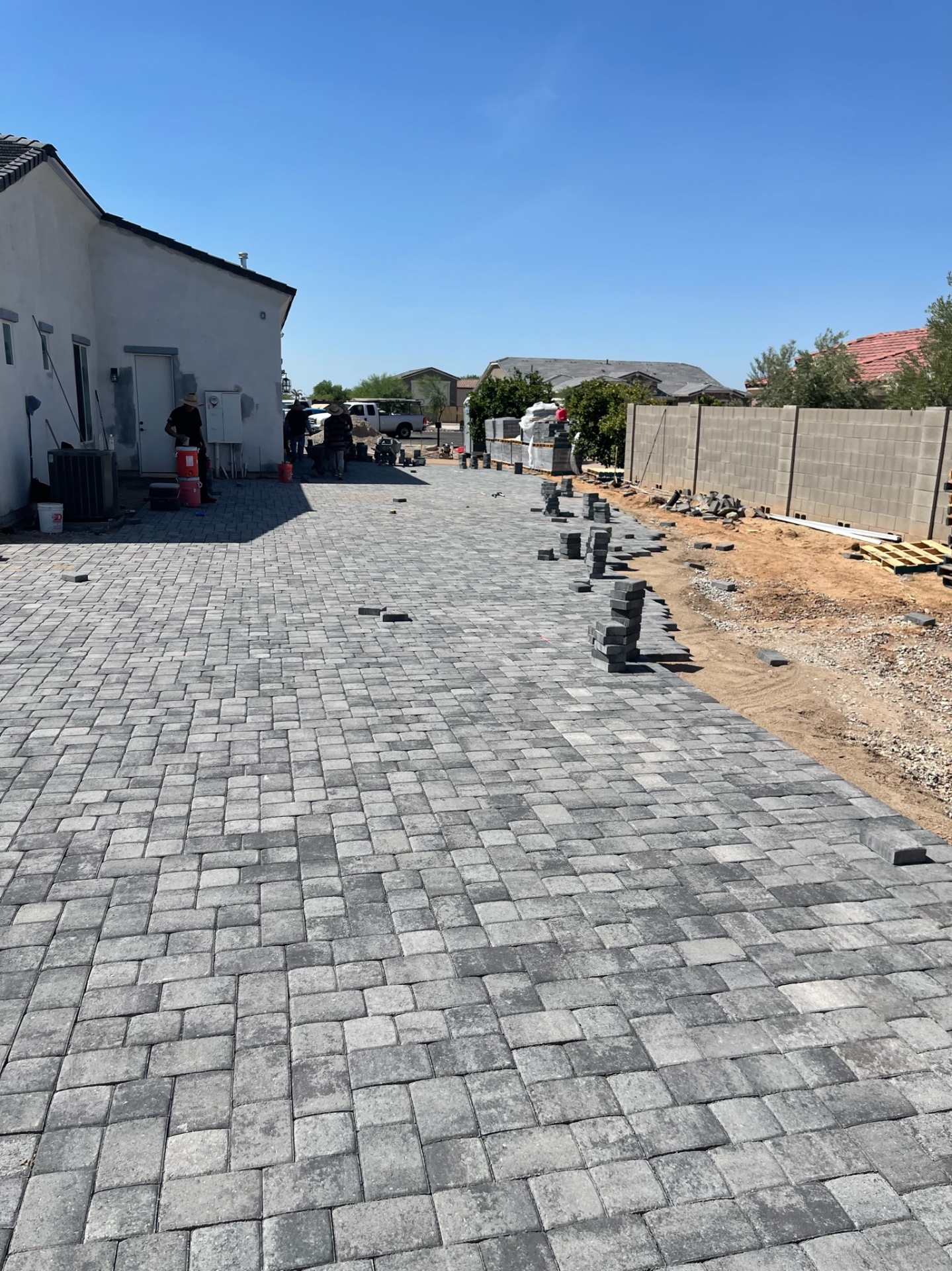 Waddell (Surprise-area) 12,000 sq ft charcoal-blend paver side-yard run in progress with AE Outdoor Living crew laying field pavers on screeded sand base, soldier-course border along block wall