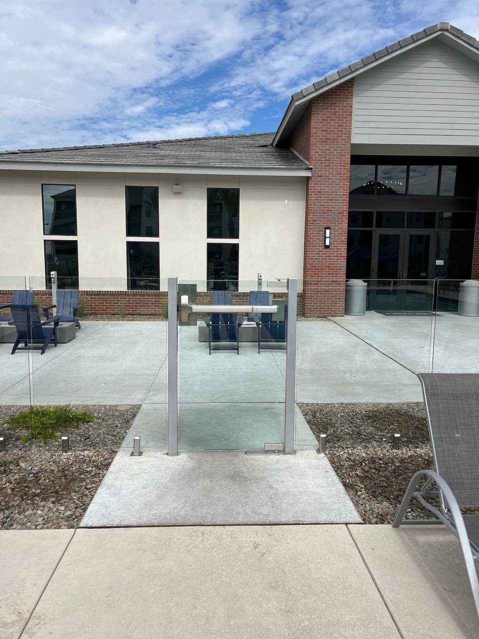Glass entry gate with a closer arm and latch hardware at a multifamily amenity area.