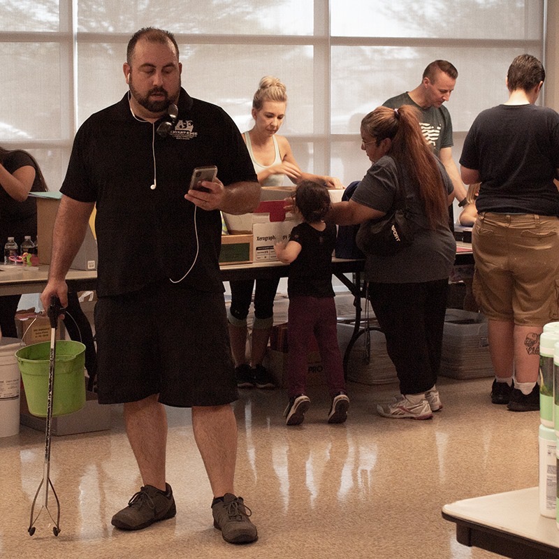 Anthony from AE Outdoor Living checking his phone while volunteers pack supplies in the background