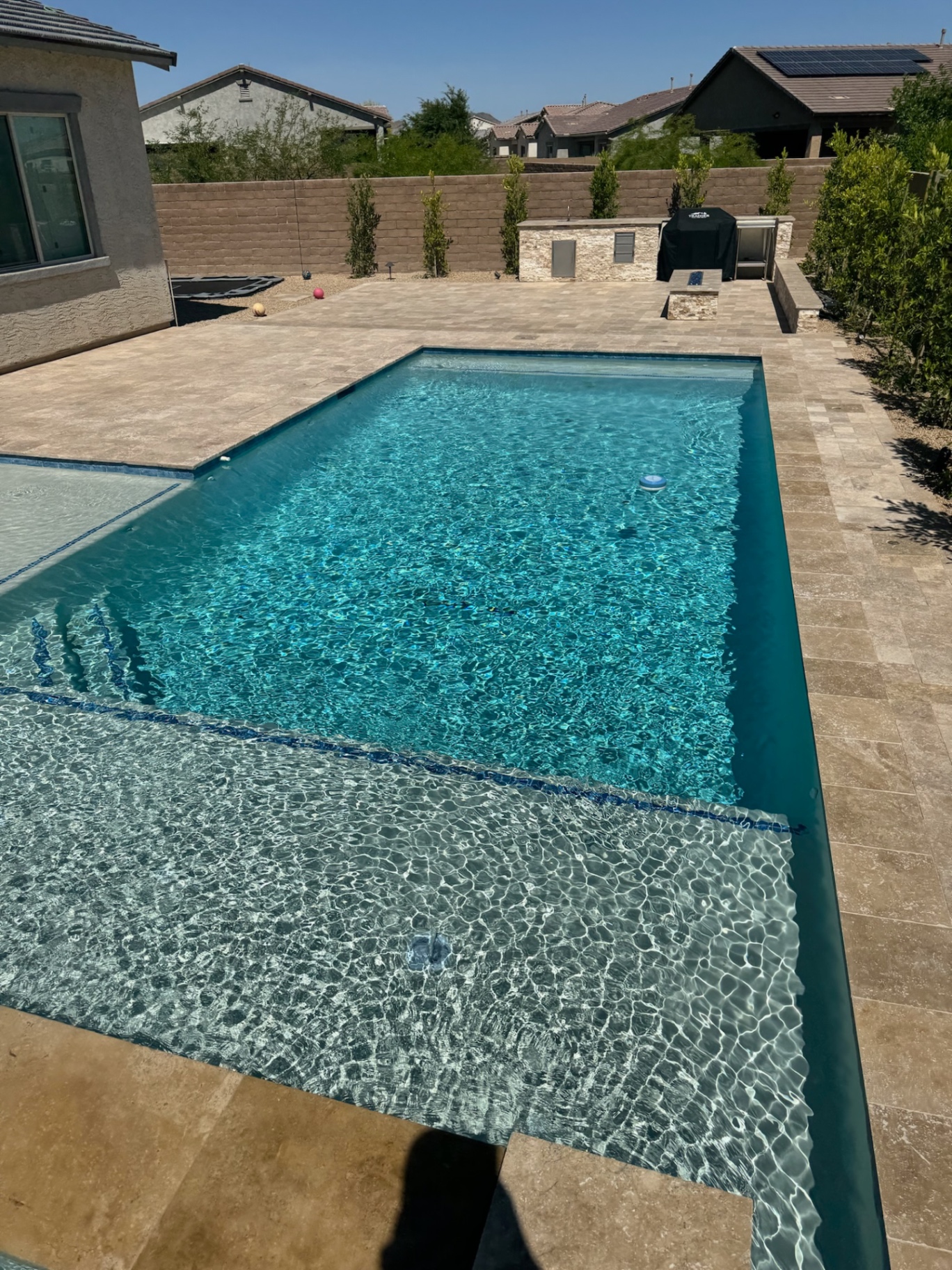 Peoria backyard pool with baja shelf, blue-glass waterline tile and paver-decked outdoor kitchen area