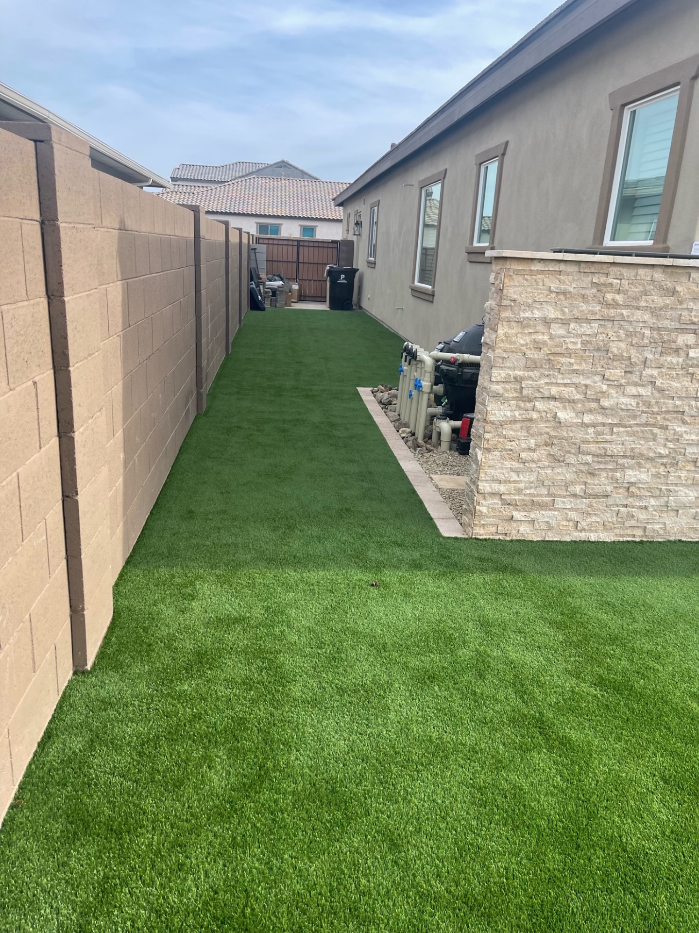 Peoria side-yard artificial turf runway with stacked-stone pool equipment enclosure, travertine paver border and desert cobble drainage