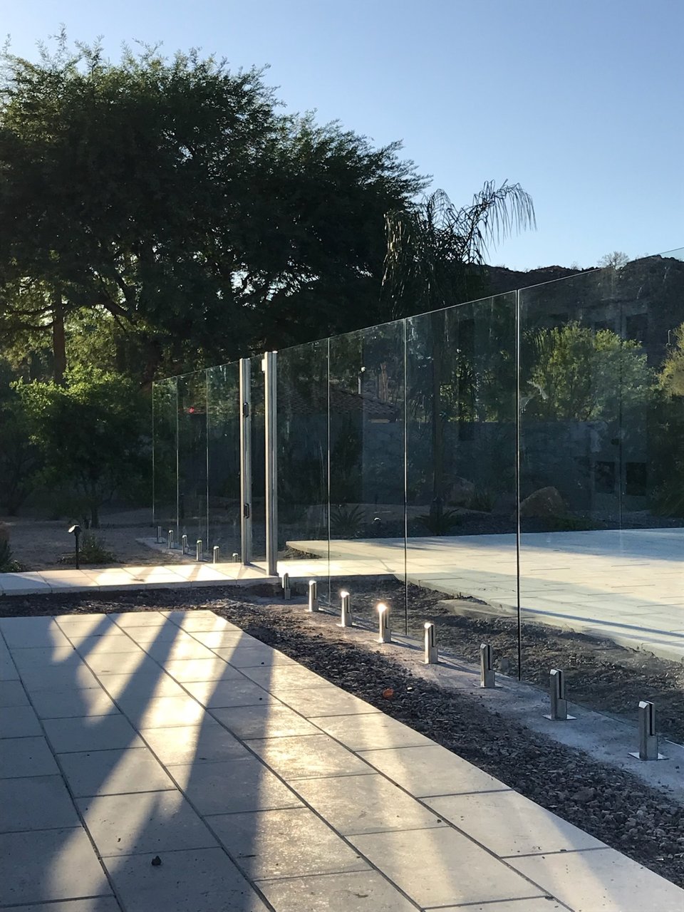 Long line of frameless glass fencing and brushed metal gate hardware lit by deck up-lighting at an estate property.
