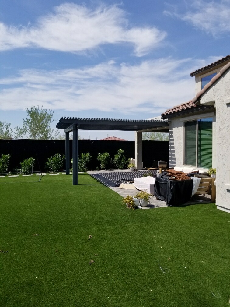 The Meadows (Peoria) L-shaped grey alumawood pergola wrapping the rear corner of a two-story home with tile-paver patio and full artificial turf lawn by AE Outdoor Living