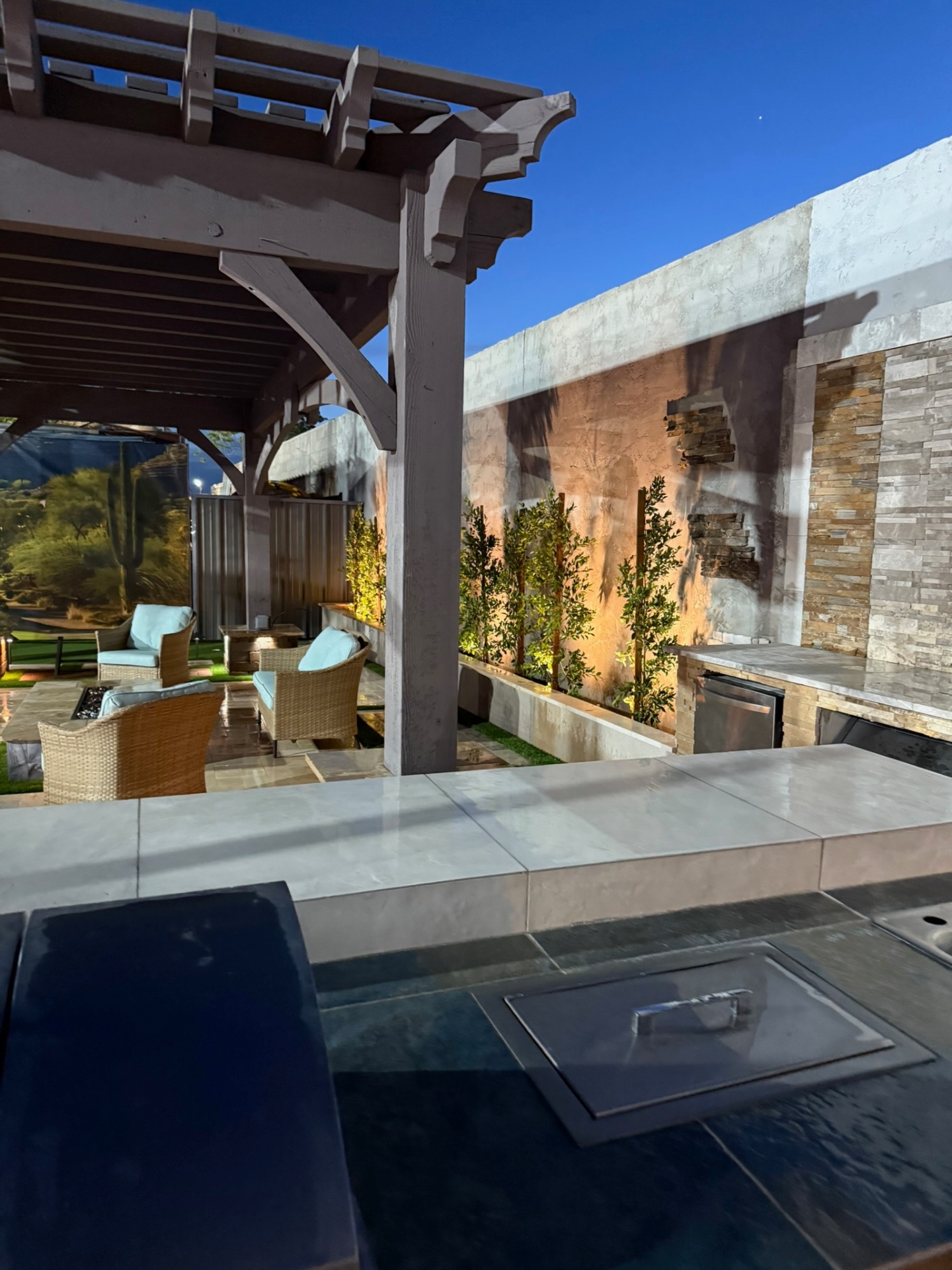 Pergola with outdoor kitchen counter, stacked stone wall, and uplit planter