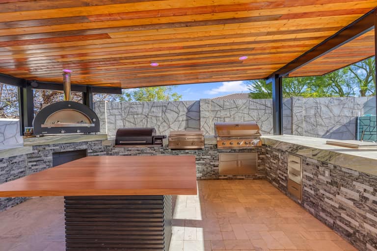 Outdoor kitchen and dining table beneath a wood-finished pavilion ceiling in Litchfield Park.