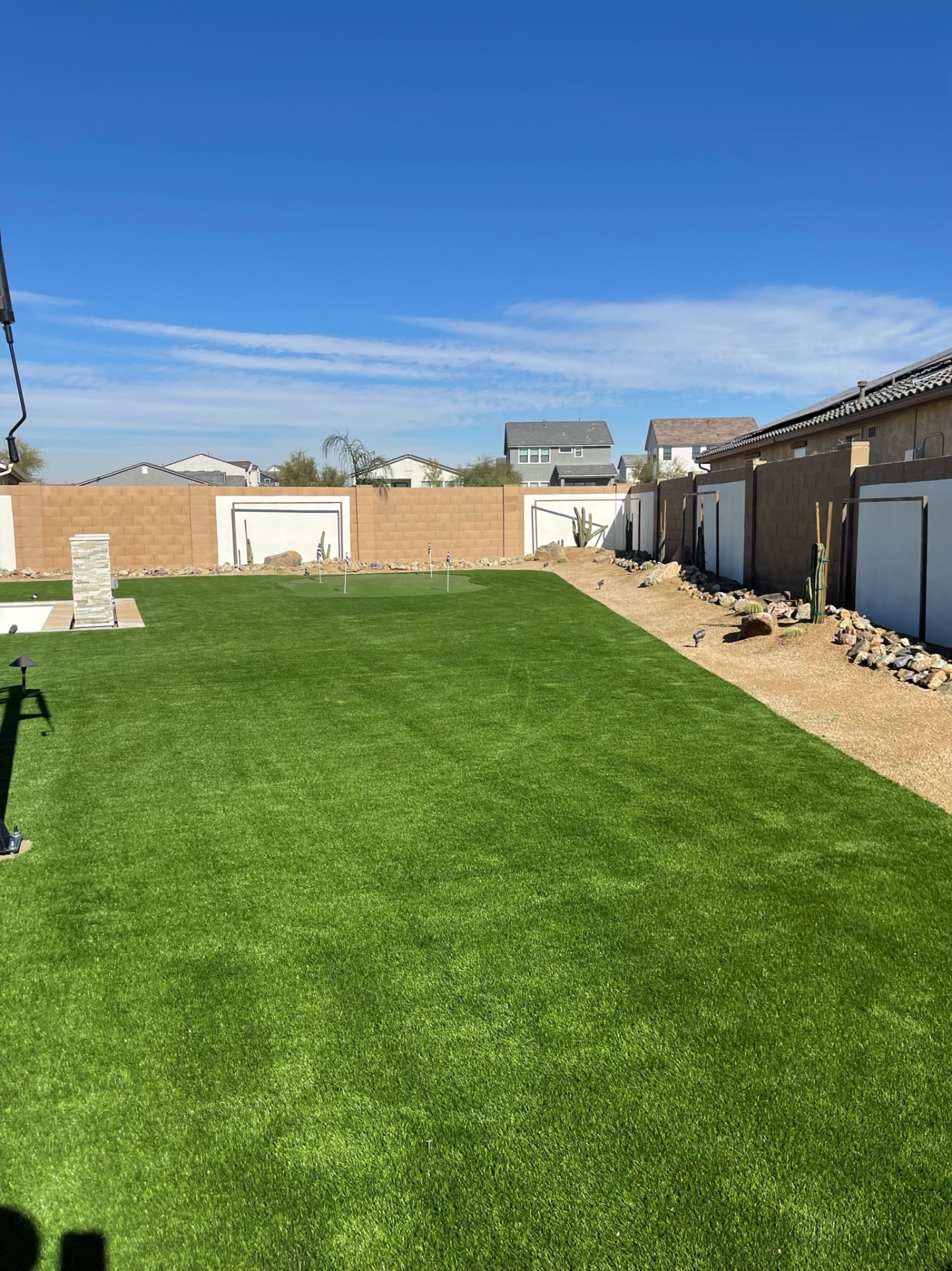 Goodyear expansive backyard artificial turf lawn with putting green, desert rock border and paver patio edge