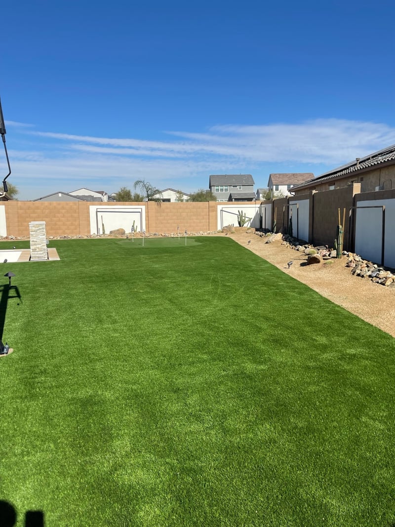 Goodyear expansive backyard artificial turf lawn with putting green, desert rock border and paver patio edge