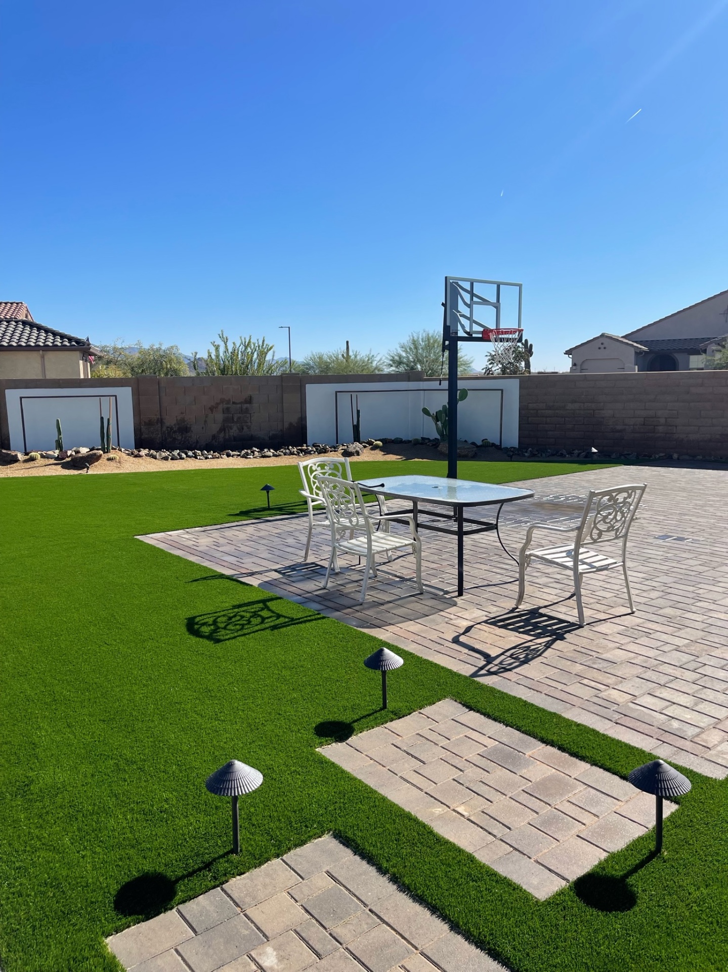 Goodyear artificial turf lawn with in-ground basketball hoop, paver dining patio and desert cactus border under blue sky