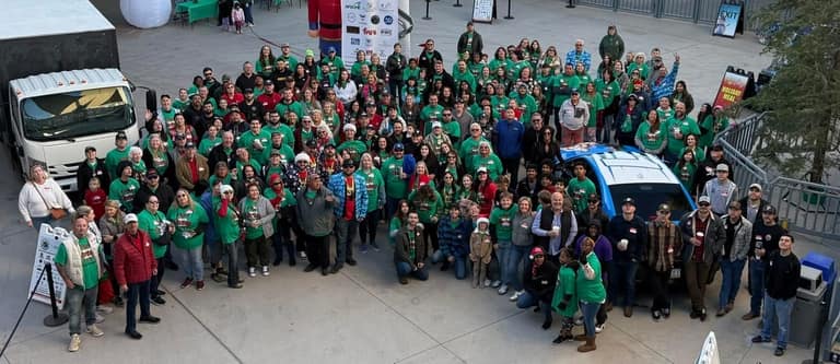 Aerial group photo of volunteers and sponsors in green shirts at A Day of Giving 2025 at Peoria Sports Complex