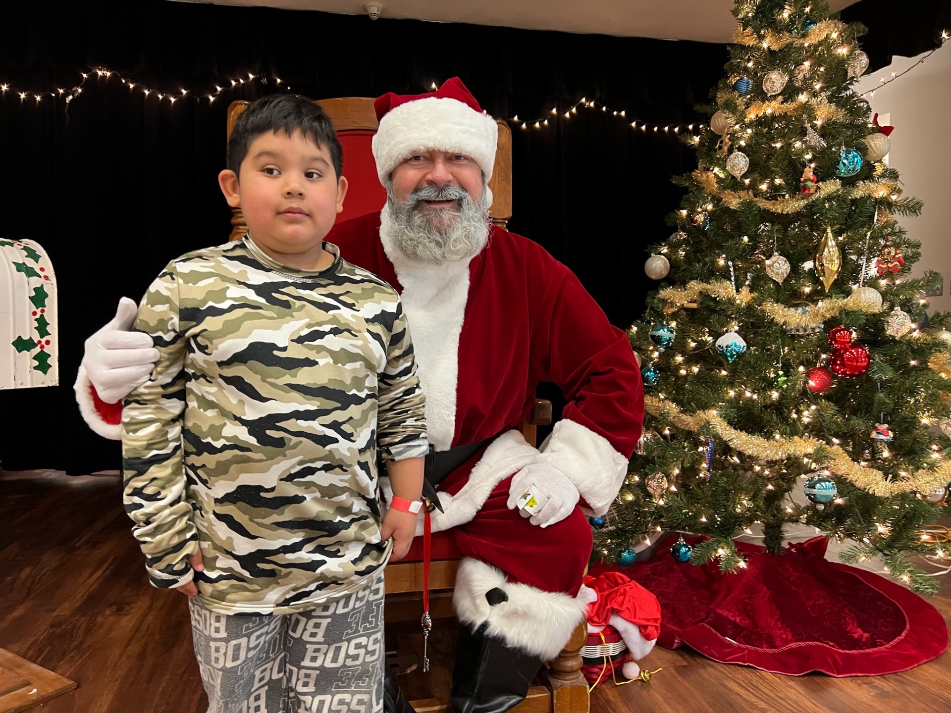 Boy in camo shirt giving a thumbs up next to Santa at Shop With a Cop