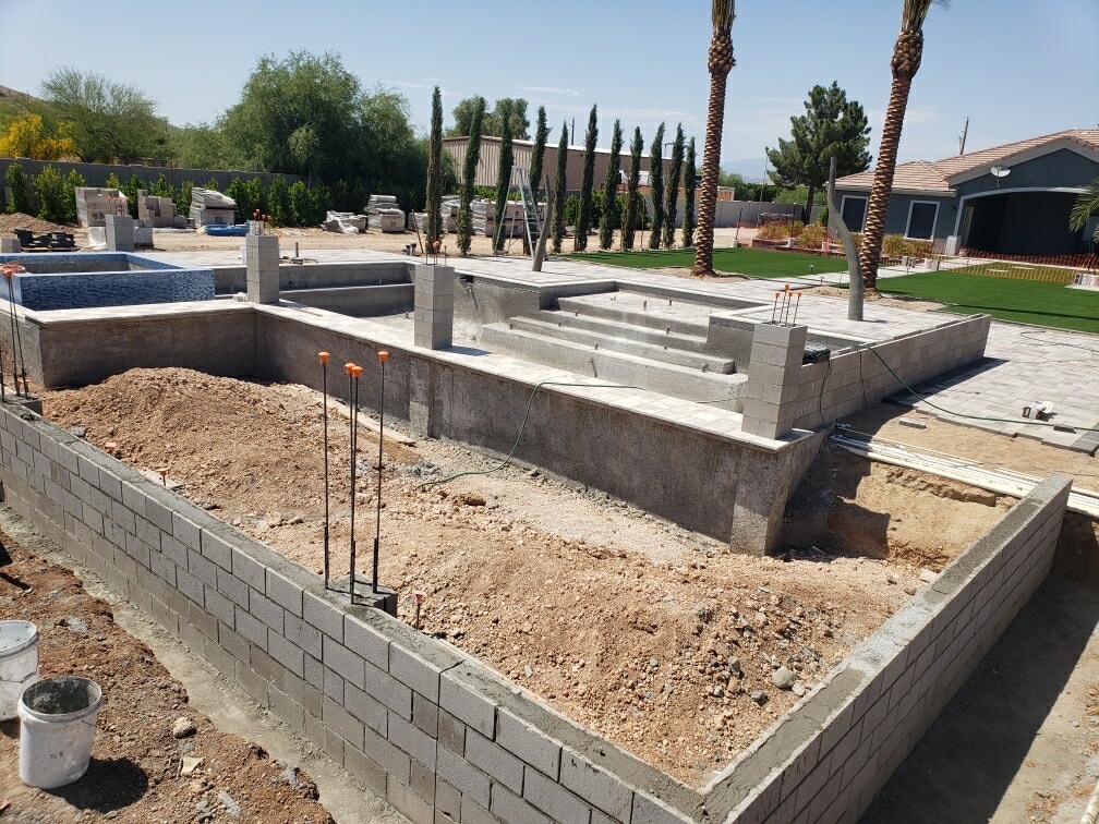 Backyard overview showing finished pool deck, raised spa, and perimeter walls awaiting backfill
