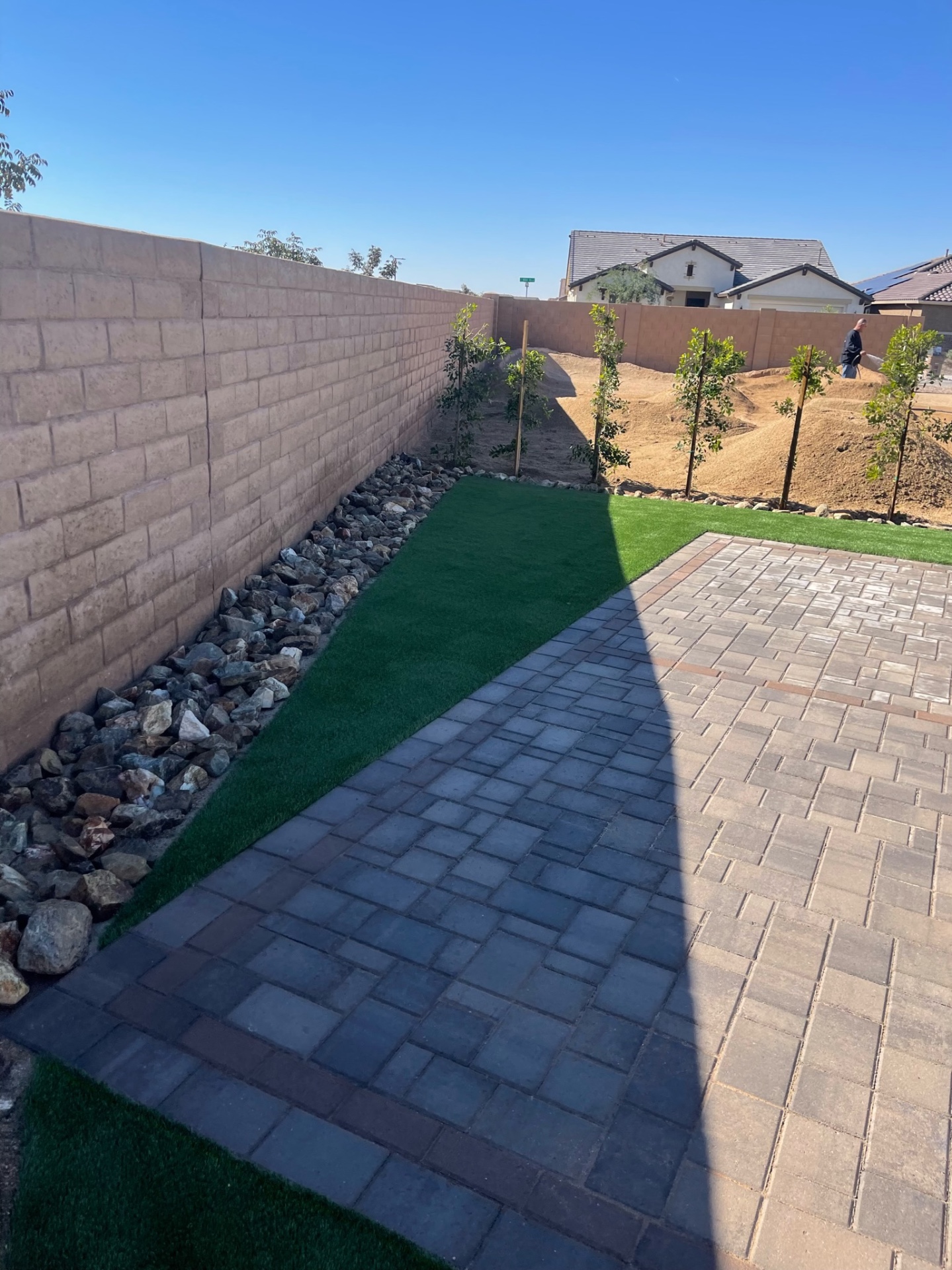 Goodyear backyard paver patio with artificial turf edge, rip-rap drainage border and freshly planted privacy trees