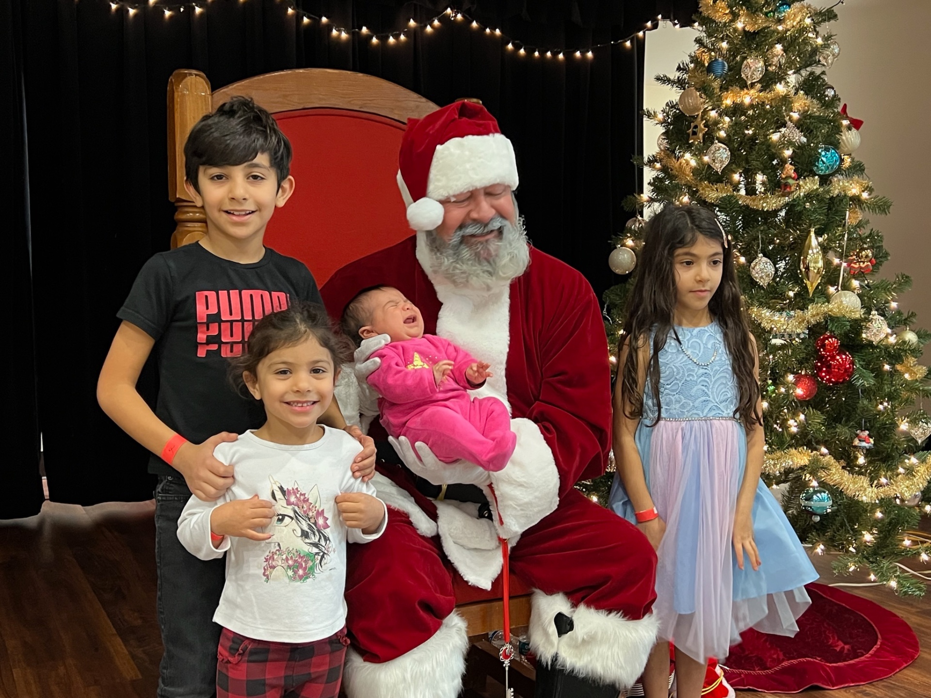 Santa holding a newborn in pink alongside three siblings at Shop With a Cop