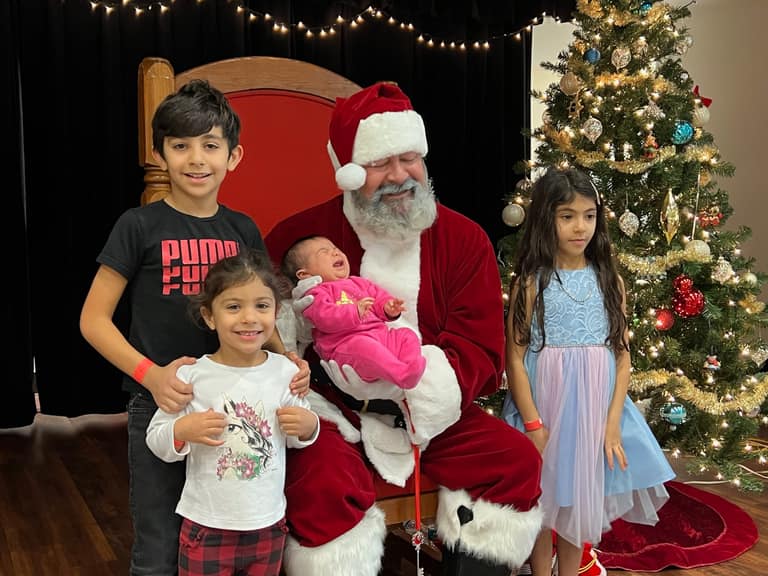 Santa holding a newborn in pink alongside three siblings at Shop With a Cop