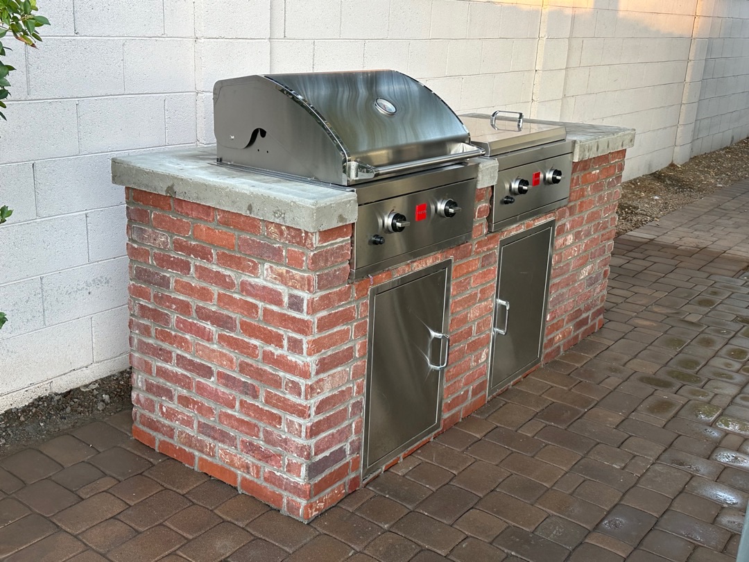 Built-in outdoor kitchen with BBQ island, stone veneer, counter, storage, and low-voltage lighting