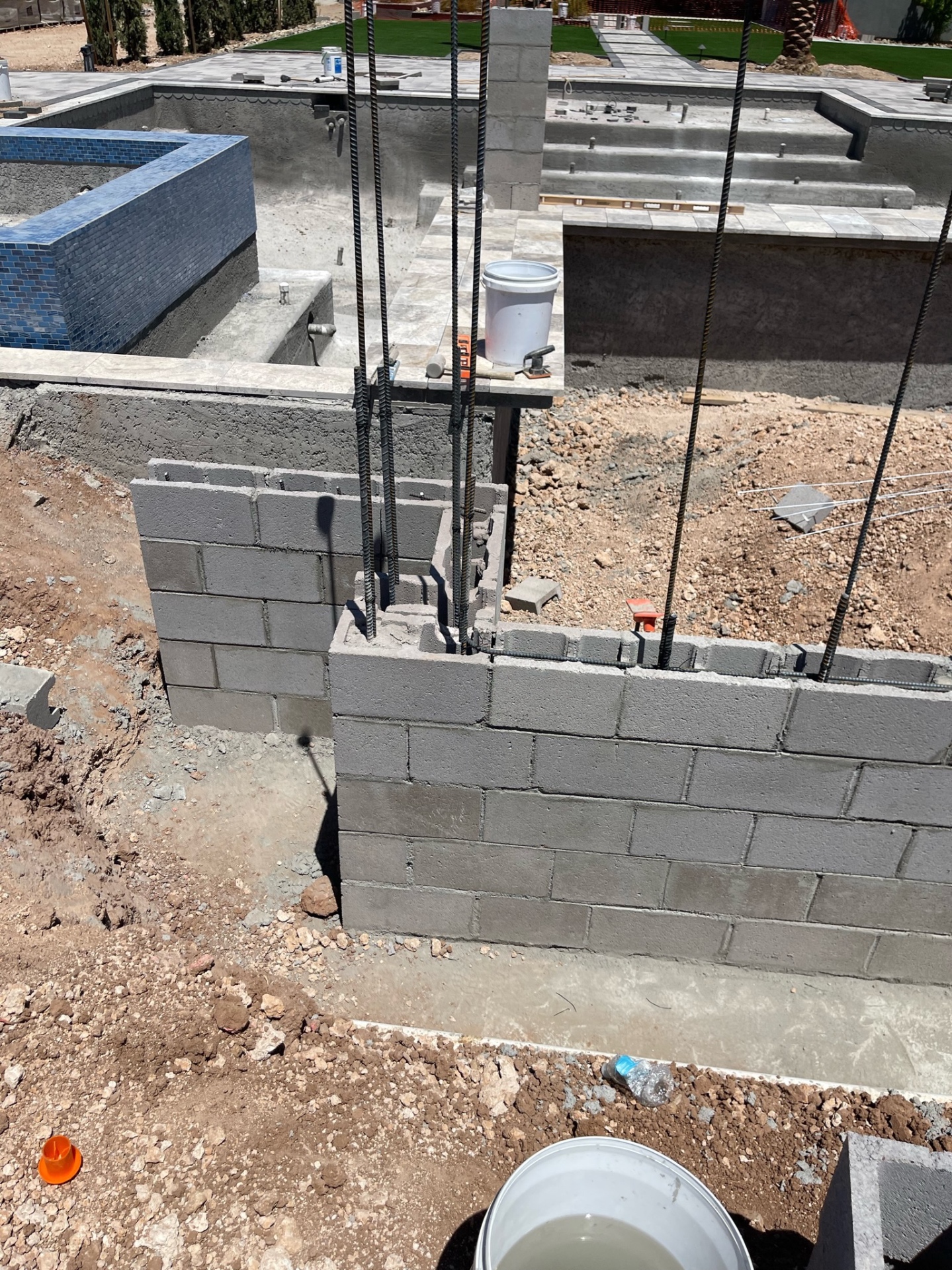 Close-up of fresh CMU corner with tall rebar dowels, pool shell and tiled spa visible beyond