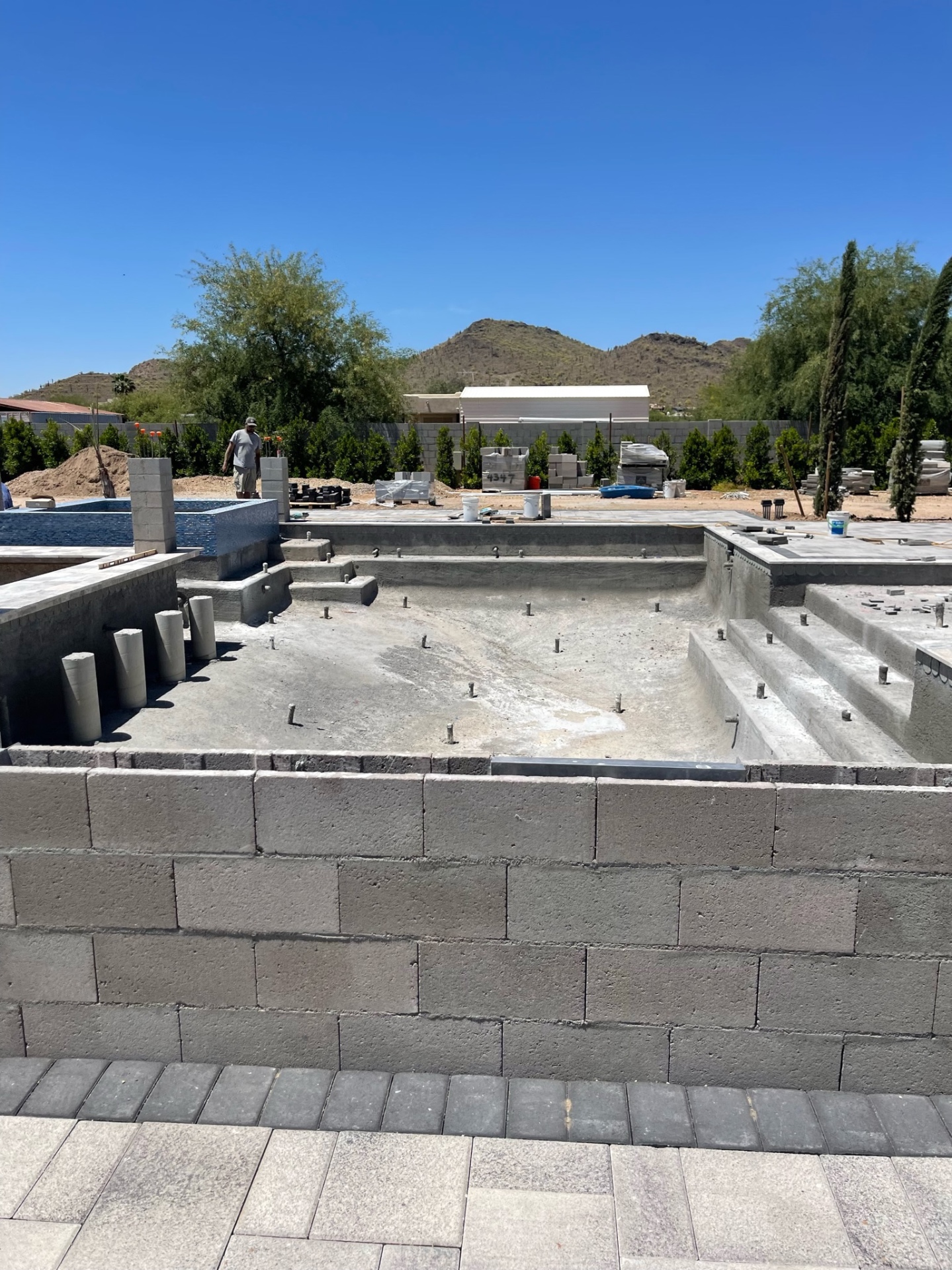 Gunite pool shell with formed steps, benches, and rebar dowels, raised tiled spa visible at far end with mountains beyond