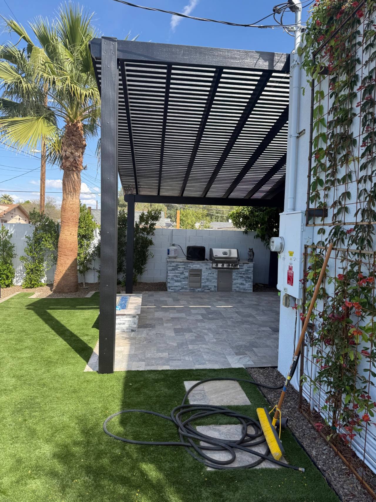 Black pergola framing an outdoor kitchen and paving court in a compact urban yard.