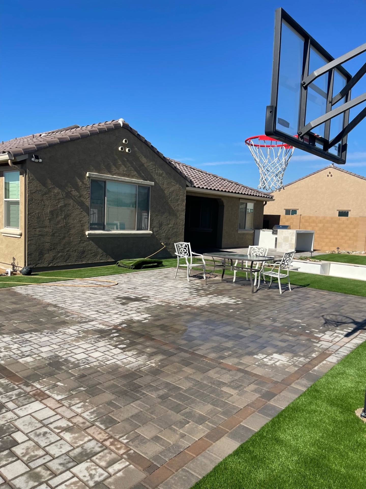 Goodyear backyard paver patio with in-ground basketball hoop, dining set, artificial turf border and built-in BBQ island beyond